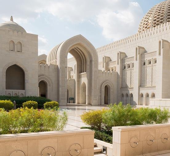 Sunlit mosque courtyard with gardens and carved stone arches